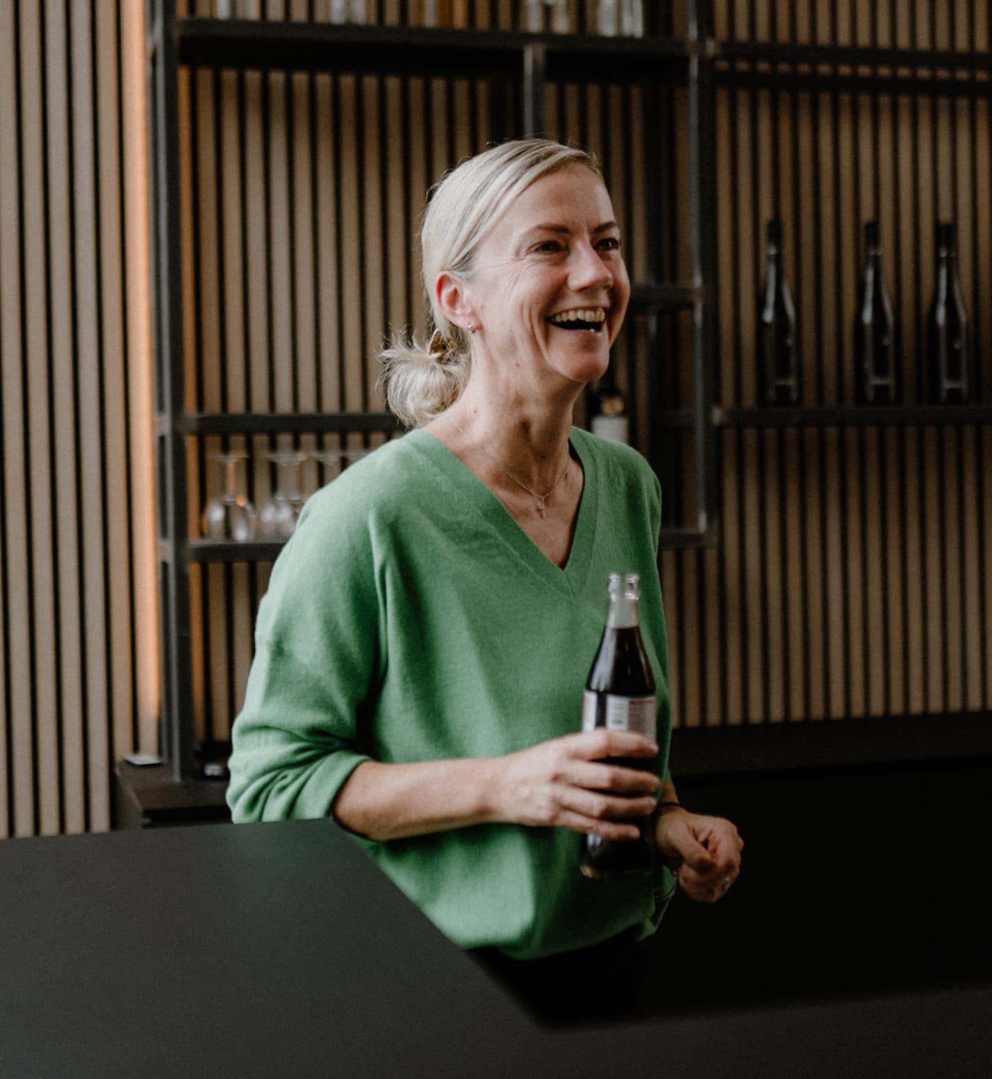 Eine Frau hat ein Getränk in der Hand und lacht.