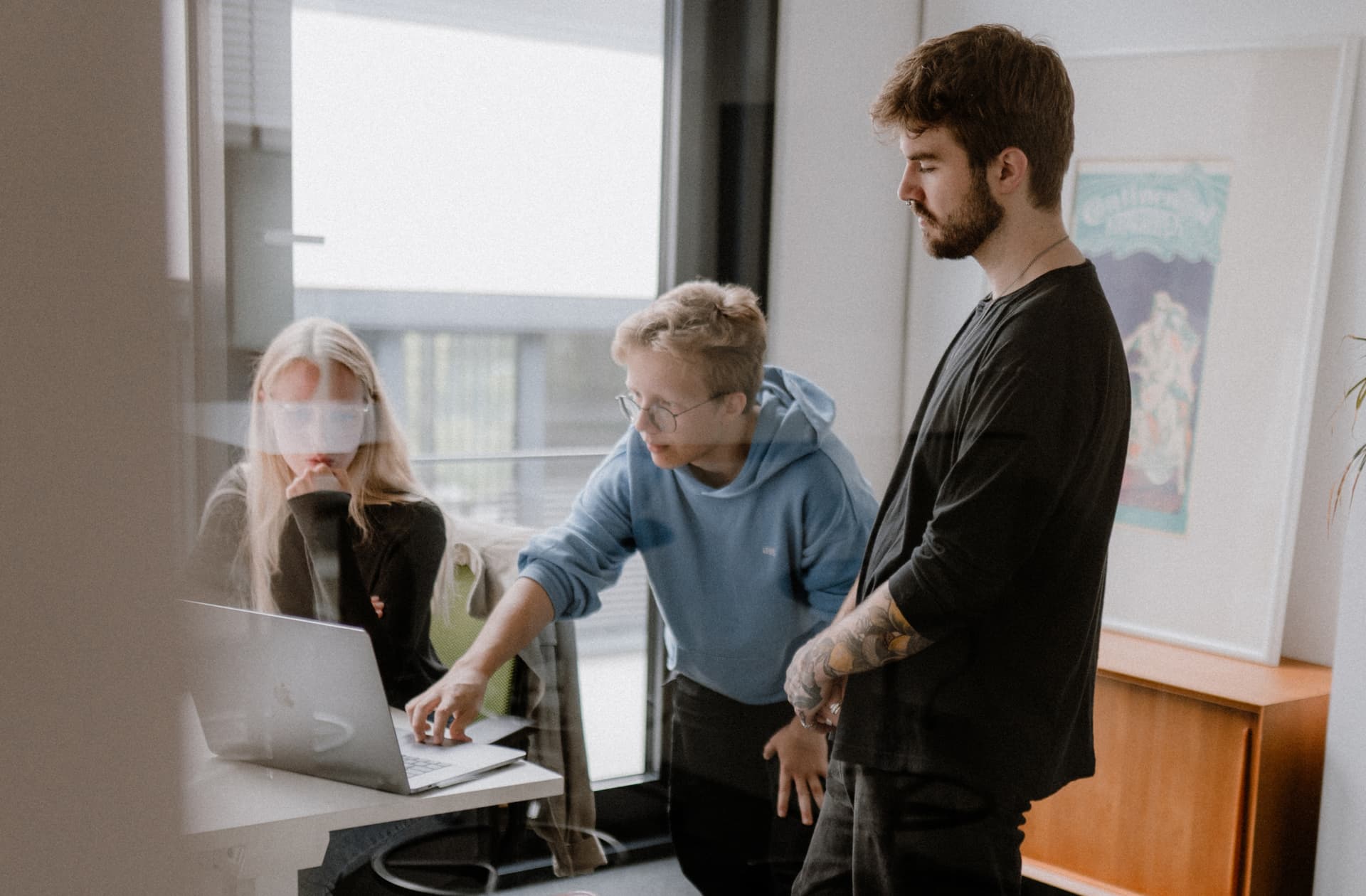 Drei junge Menschen betrachten einen Laptop und unterhalten sich.